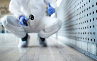 Person in white protective suit using a sprayer for disinfection in public area.