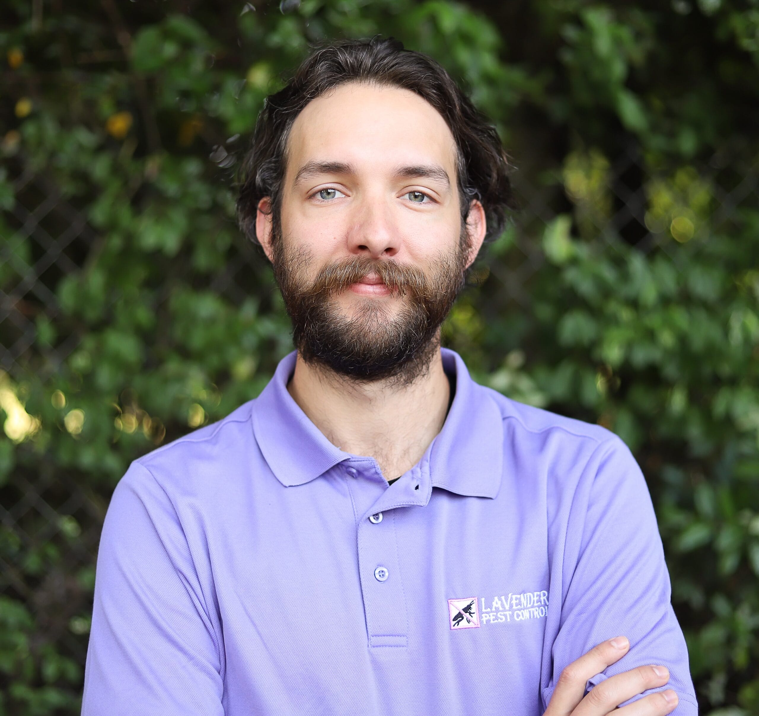 Person in lavender pest control uniform with greenery in the background.