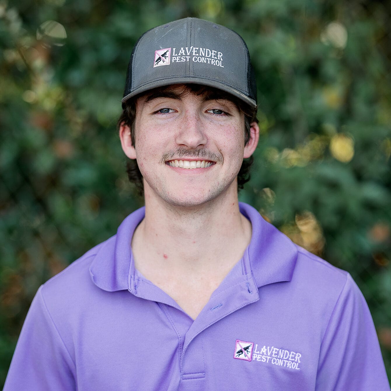 Young man in Lavender Pest Control uniform and cap, smiling outdoors.
