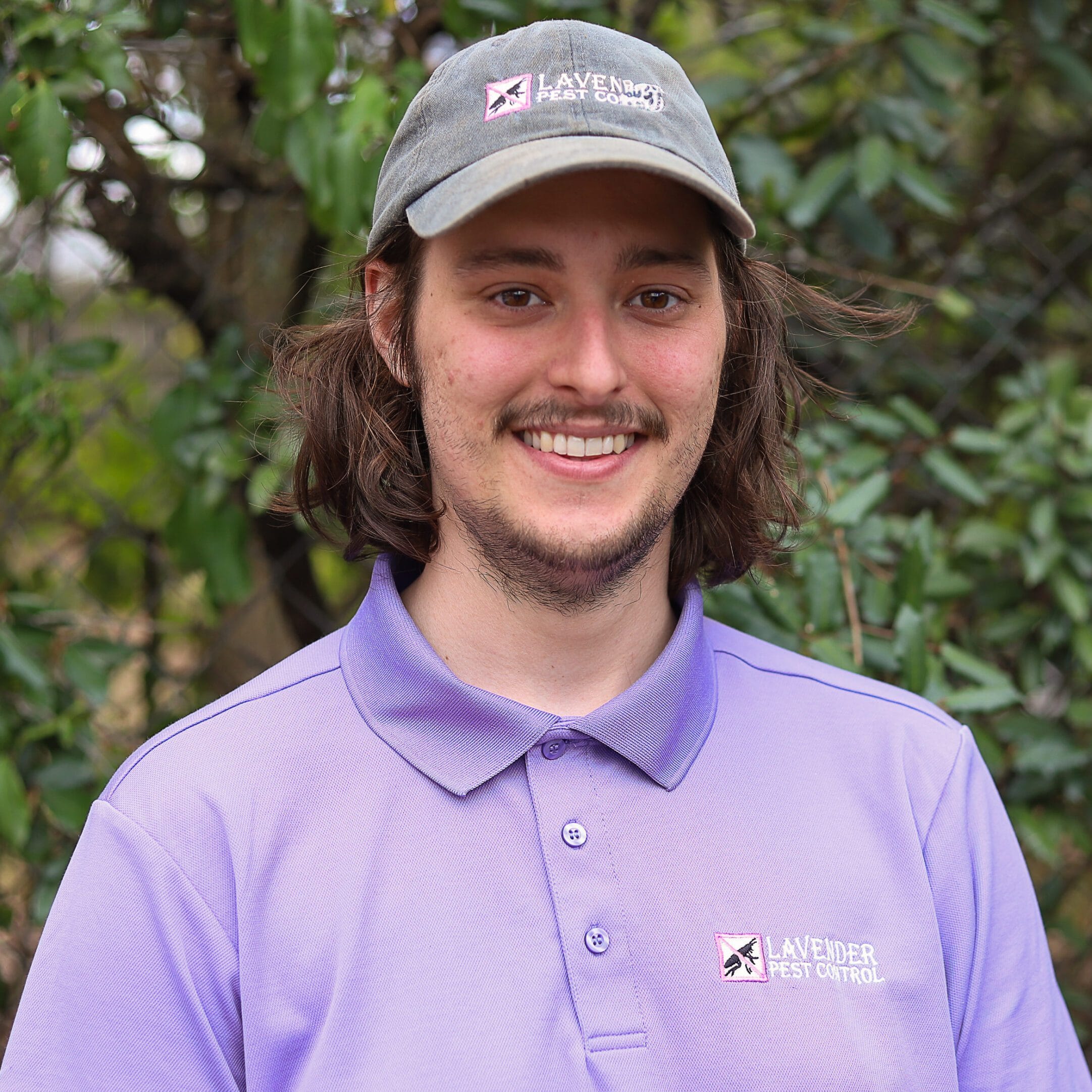 Person in lavender pest control uniform smiling in a garden setting.
