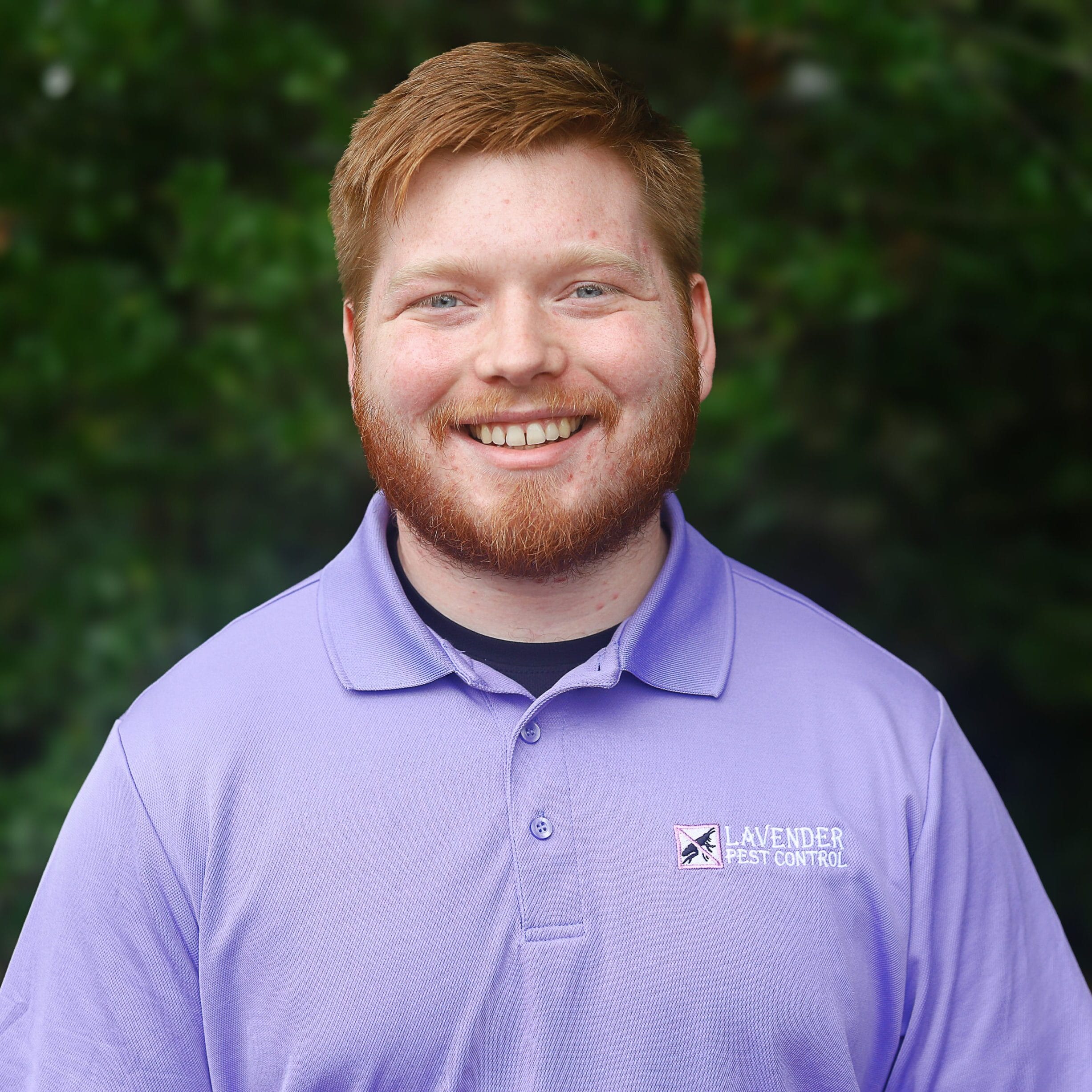 Smiling individual in a Lavender Pest Control uniform with a nature backdrop.